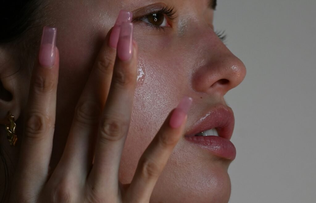 A close-up profile of a person with glowing, hydrated skin gently pressing a clear, lightweight skincare product, like a serum or essence, into their cheek using their fingertips.