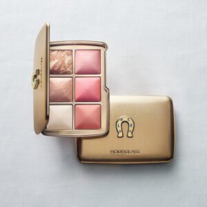 A gold Hourglass limited-edition Luck Palette from the 2026 Holiday collection. An open compact displaying six ambient lighting face powders rests on top of a closed compact featuring a raised horseshoe emblem with the word LUCK.