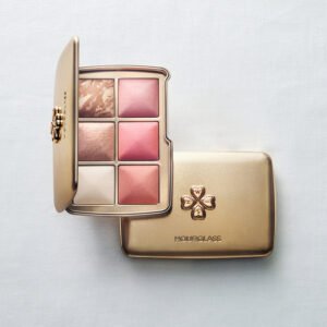A gold Hourglass limited-edition Holiday Ambient Lighting Edit face palette, open to reveal six baked powders, resting on top of a closed gold palette featuring a raised, ornate hourglass design.