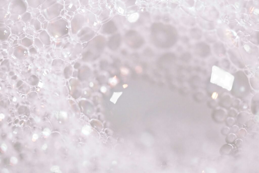 A macro close-up of white, airy soap bubbles and frothy lather, resembling a foaming skincare cleanser.